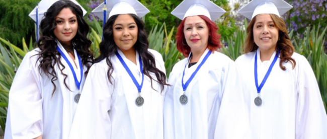 Four adult women in white caps and gowns